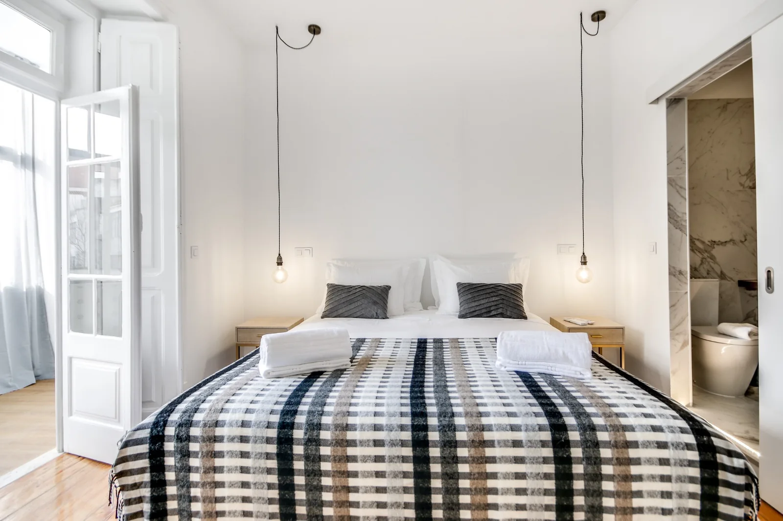 Quarto com cama de casal, roupa de cama aos quadrados e casa de banho